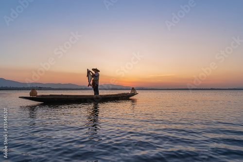 Picture of Asian fishermen on a wooden boat Thai fishermen catch fresh water fish in the natural river  traditional Thai fishermen at the morning sun on the lake of Thailand