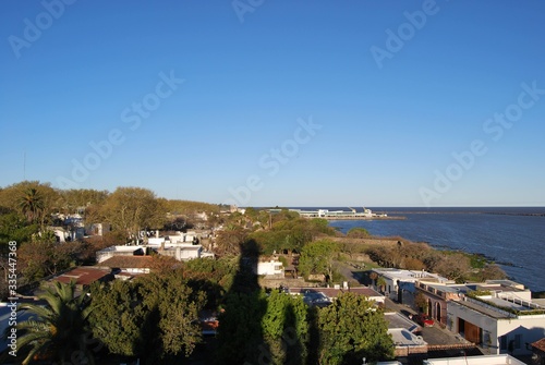 Ciudad, arboles y rocas cerca al mar, cielo despejado. 