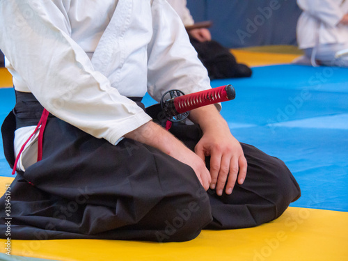 Man sitting on the tatami with japanese sword. Martial arts instructor with katana on seminar sitting in position seiza. View of front.