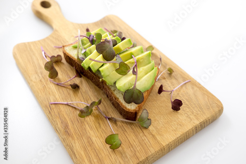 Radish microgreens as garnish on sliced avocado with gluten free bread on a board