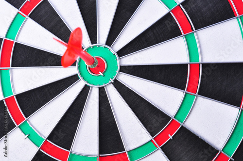 Red dart arrow hitting in the target center of dartboard