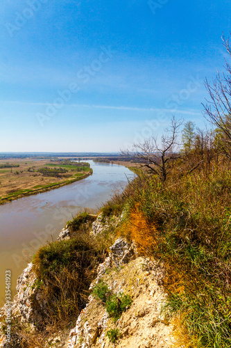Top view of the bend of the river, two banks, bare branches against the blue sky on a spring day