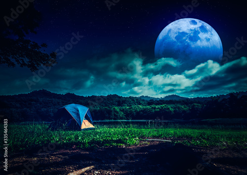 Great view of camping tent near lake at night with many stars and full moon. The concept of travel, tourism, camping.