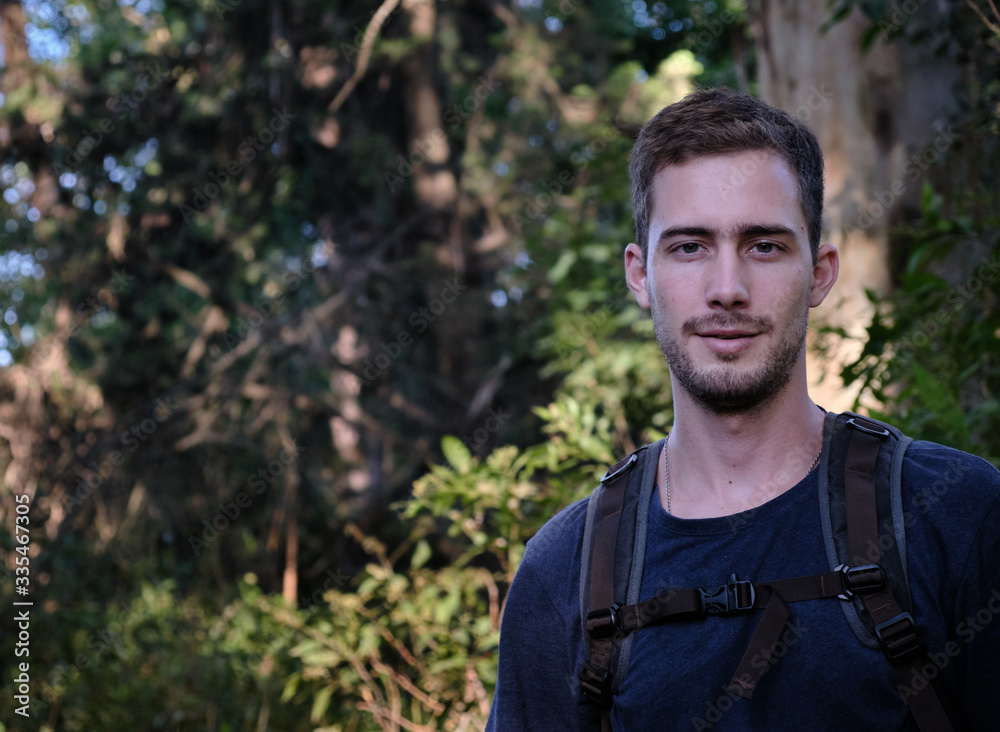 a model man dressed as a hiker or walker with a technical bag over a background of trees and branches of a forest a model man dressed as a hiker or walker with a technical bag over a background of trees and branches of a forest