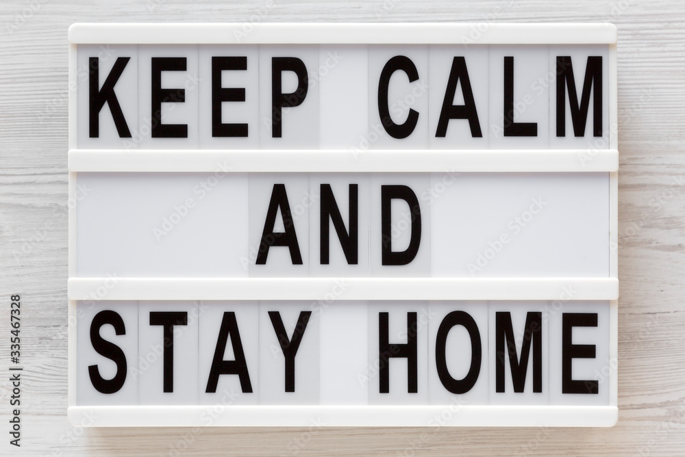 Fototapeta premium 'Keep Calm and Stay Home' words on a lightbox on a white wooden background, top view. Overhead, from above, flat lay.