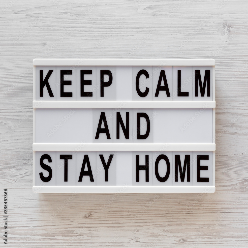 'Keep Calm Stay Home' words on a lightbox on a white wooden surface, top view. Overhead, from above, flat lay. 'Keep Calm Stay Home' words on a lightbox on a white wooden surface, top view. Overhead, from above, flat lay.