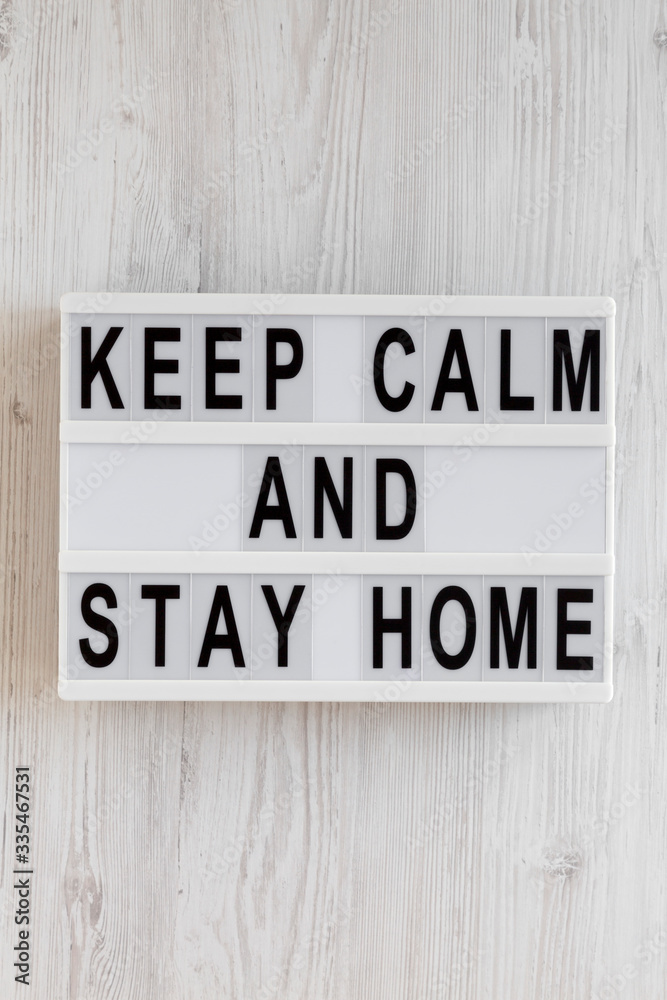 'Keep Calm and Stay Home' words on a lightbox on a white wooden surface, top view. Overhead, from above, flat lay. 'Keep Calm and Stay Home' words on a lightbox on a white wooden surface, top view. Overhead, from above, flat lay.