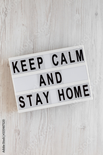 'Keep Calm and Stay Home' words on a modern board on a white wooden surface, top view. Overhead, from above, flat lay.