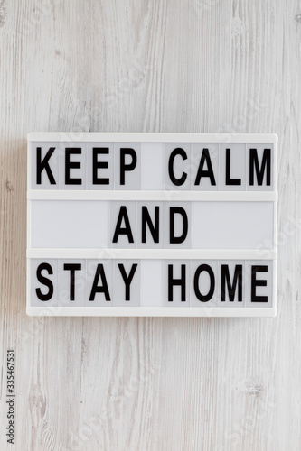 'Keep Calm and Stay Home' words on a lightbox on a white wooden surface, top view. Overhead, from above, flat lay.