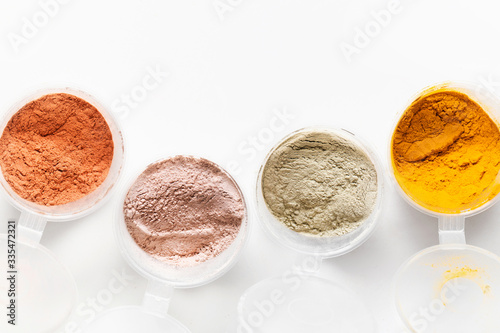 A top view of the loose pigments and powders in circle plastic jars on white background. Food and cosmetic colorful organic ingredients. Close-up