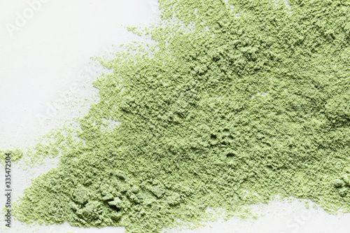 A top view of a loose green cosmetic or food powder pigment on a white background. Matcha tea. Colorful texture. Copy space. Close-up