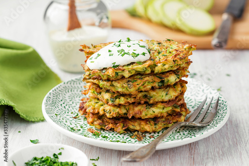 Foto Zucchini fritters, vegetarian zucchini pancakes, served with fresh herbs and sour cream
