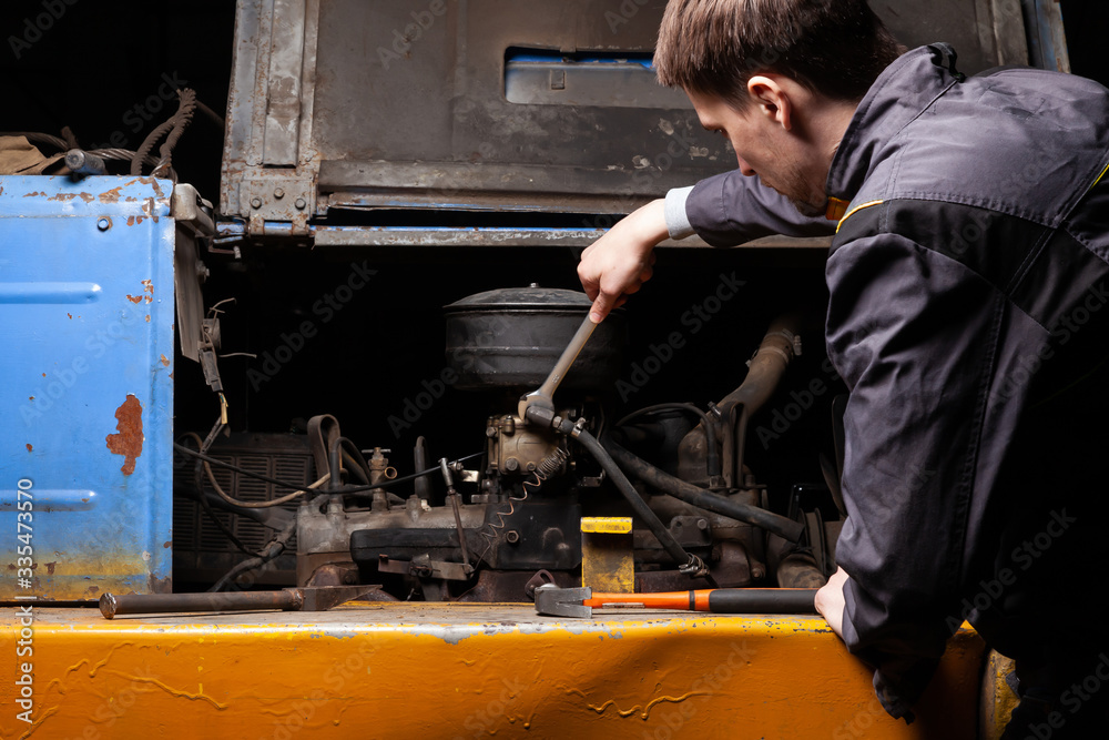Φωτογραφία A male mechanic is repairing the engine of an old truck with an open hood with a wrench
