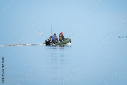 Two fishermen motoring infladable boat with outboard motor on the very calm lake with infinite look. Kama river (Niznekamsk Reservoir), Russia photo