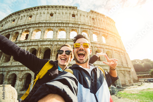 Happy caucasian couple is taking a selfie smiling at the camera in front of the colosseum in Rome 