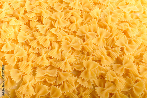 Heap of dried Farfalle Rigate Italian pasta ready to be cooked, isolated on a white table, top view or flat lay of healthy food 

