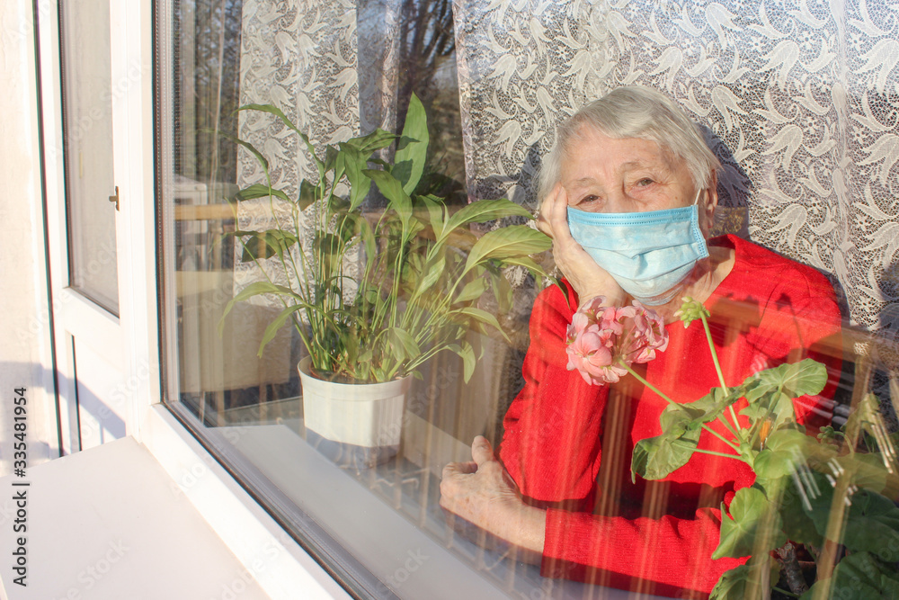 Fototapeta premium The Covid-19, health, safety and pandemic concept - senior old lonely woman sitting near the window