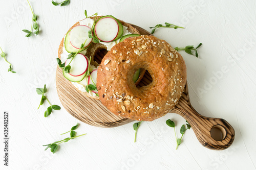 bagel with cream cheese, radish, cucumbers and pea seedlings on a white plate