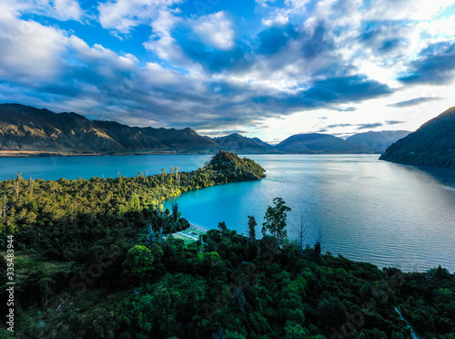 Green lush Forest peninsula on Lake Wakatipo with Southern Alps mountains in the background, aerial view at sunset