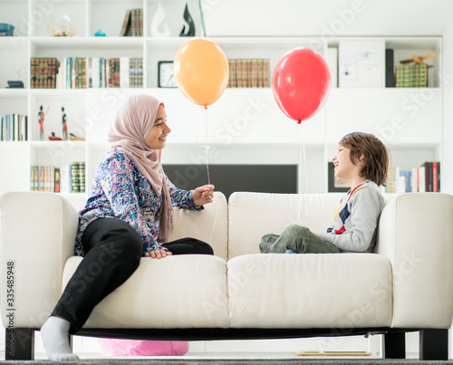 Muslim woman and little boy playing with balloons at home