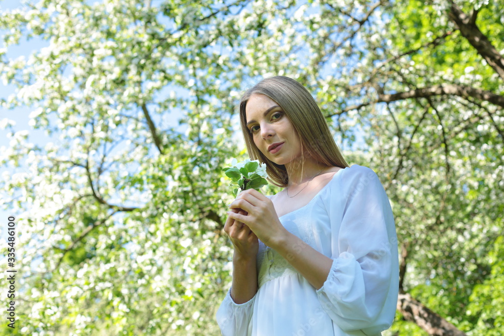 Happy blonde woman on a background of blooming spring garden with her hands raised to the sky Happy blonde woman on a background of blooming spring garden with her hands raised to the sky