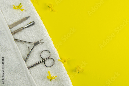 A set of cosmetic tools for manicure and pedicure. Manicure scissors, cuticles, saws on white towel stand on a yallow background. Top views with clear space photo