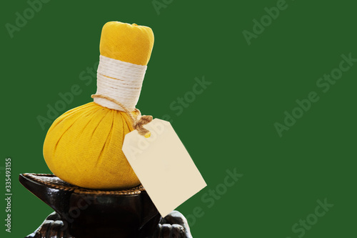 The picture of a yellow traditional fresh Thai herbal compress ball with black paper label on green background