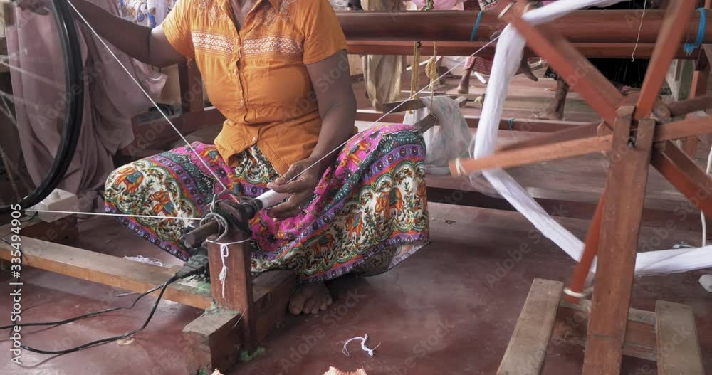 Hands of an old woman using an old spinning wheel to turn wool into yarn
