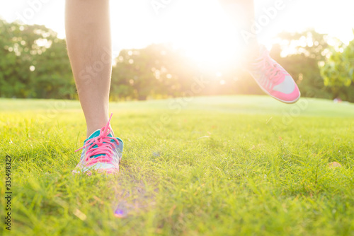 Foot of sport women running on green grass field in oark with sun light