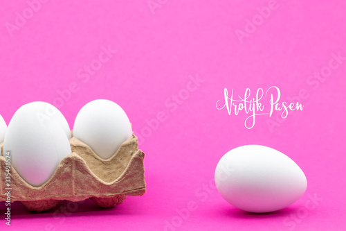 Vrolijk Pasen, Dutch words for Happy Easter on a pink background. An egg carton and one egg out of the box. Room for text.  