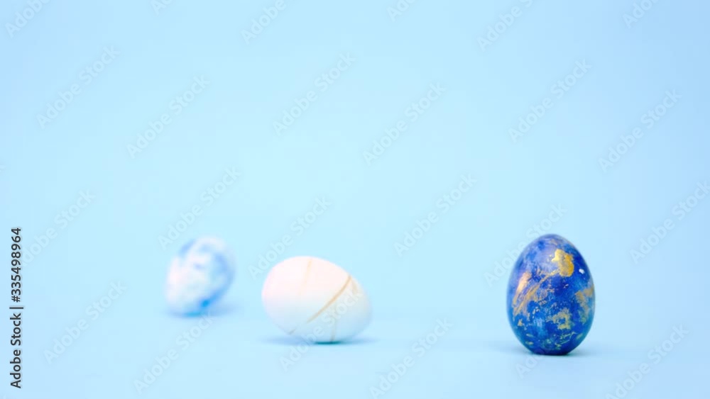 Easter eggs are rolling, knocking each other on blue table. Eggs trendy colored classic blue, white and golden . Happy Easter. Minimal style Easter eggs are rolling, knocking each other on blue table. Eggs trendy colored classic blue, white and golden . Happy Easter. Minimal style