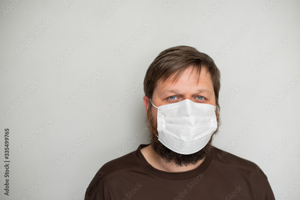 COVID-19 Pandemic Coronavirus. Portrait of a man with a beard in a white mask on a light background COVID-19 Pandemic Coronavirus. Portrait of a man with a beard in a white mask on a light background