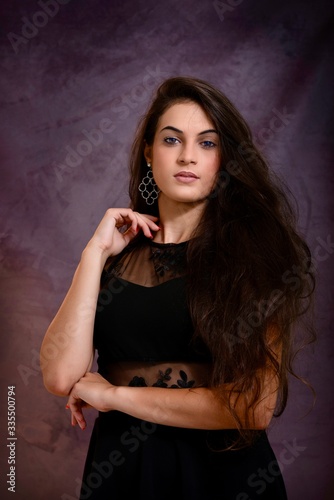 black hair woman portrait with brown eyes on a gray background , Caucasian ethnic group is looking into the camera with a serious expression on her face. White girl with long black hair and brown eye