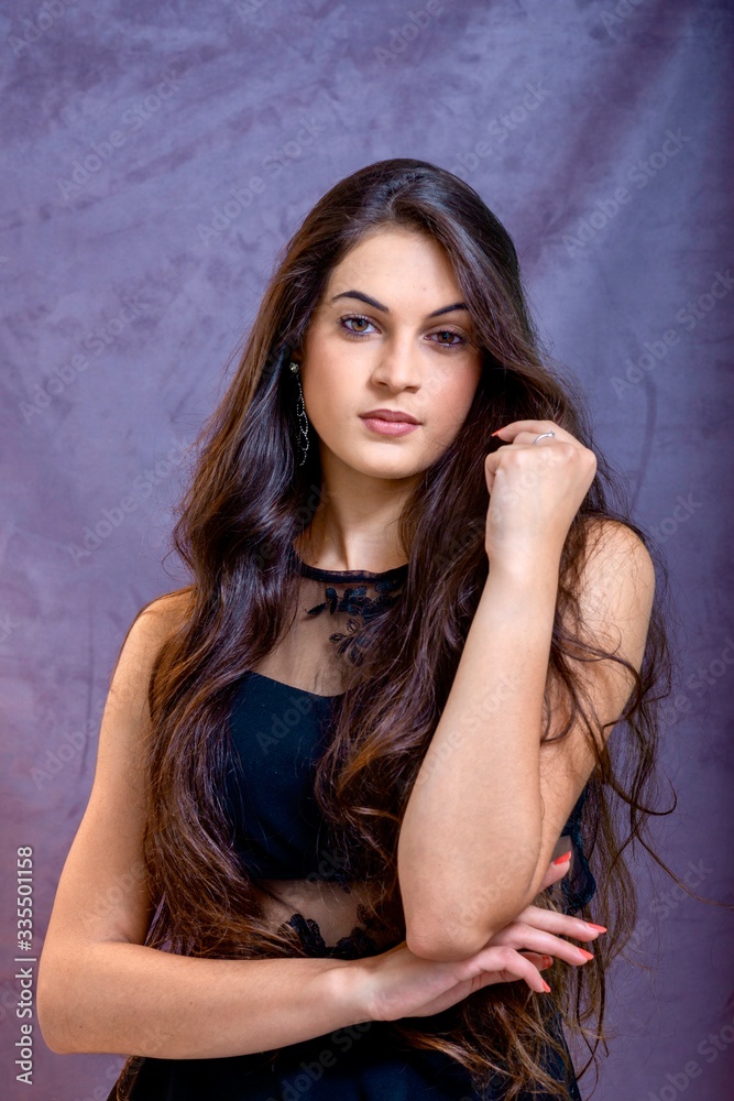 black hair woman portrait with brown eyes on a gray background , Caucasian ethnic group is looking into the camera with a serious expression on her face. White girl with long black hair and brown eye black hair woman portrait with brown eyes on a gray background , Caucasian ethnic group is looking into the camera with a serious expression on her face. White girl with long black hair and brown eye