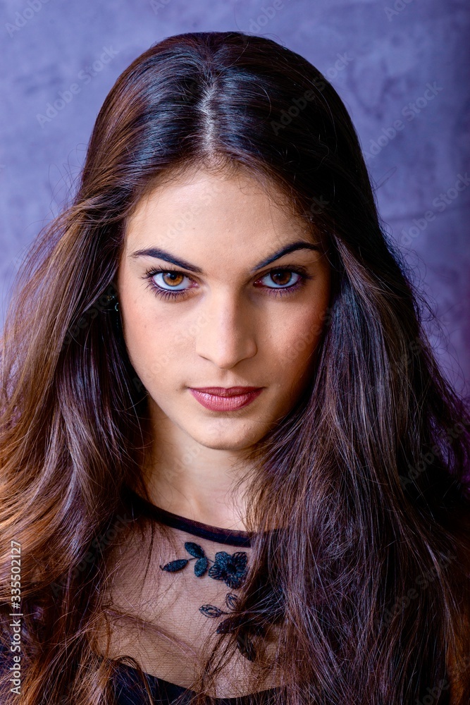 Naklejka premium black hair woman portrait with brown eyes on a gray background , Caucasian ethnic group is looking into the camera with a serious expression on her face. White girl with long black hair and brown eye