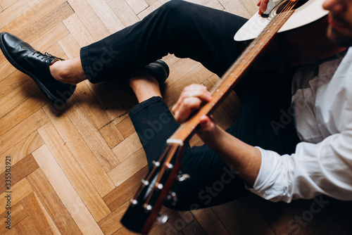 A man sits on the floor and plays guitar. Guy with guitar in his hands.