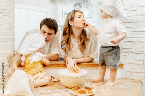 Charming two-year-old boy gives his mother a try to bake pancakes during family cooking with dad and sister. Concept of hobbies and joint developmental experiences with children
