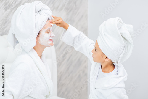 Young girl cleans her mom's face with a cotton pad and lotion
