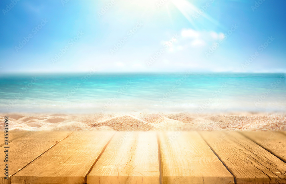 tropical summer beach with empty wooden flooring in rays of sun light on nature. Golden sand beach, ocean against blue sky with white clouds. Copy space, summer vacation concept.