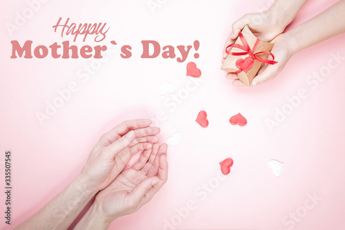 Fototapeta Naklejka Na Ścianę i Meble -  Mother's day greeting card on a pink background. Children's hands and female hands. Gift box and hearts.