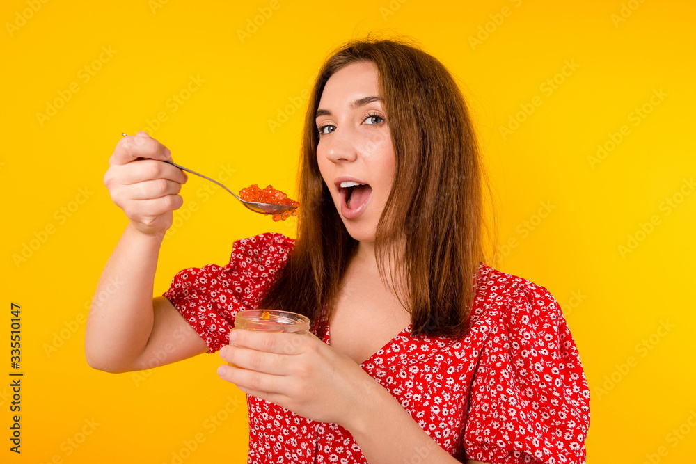 Beautiful girl on a yellow background eating red caviar with a spoon close up happy to be quarantined Beautiful girl on a yellow background eating red caviar with a spoon close up happy to be quarantined