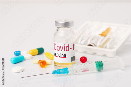 Bottle with Covid-19 vaccine and syringe between pills on white medical table. Concept of inventing vaccine to stop coronavirus pandemic