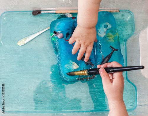 A small child is trying to get animal figures out of ice. The development of children's motor skills using a sensory box. Development of children at home during a pandemic and quarantine