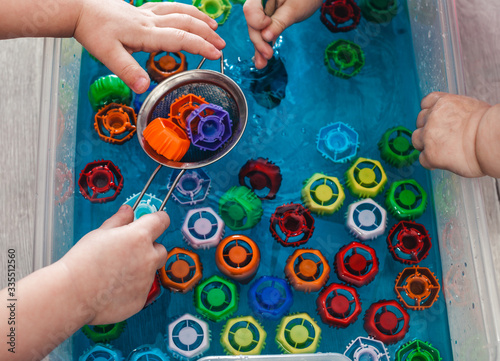 Children take out colored covers from the water. The development of children's motor skills using a sensory box. Development of children at home during a pandemic and quarantine