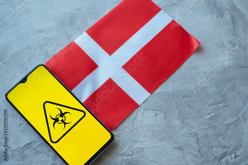 Epidemiological situation in the country Denmark. Flag and smartphone with news and a biohazard symbol.
