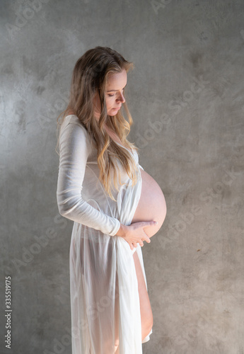 Pretty pregnant woman touching her belly while standing over gray wall background. Maternity concept