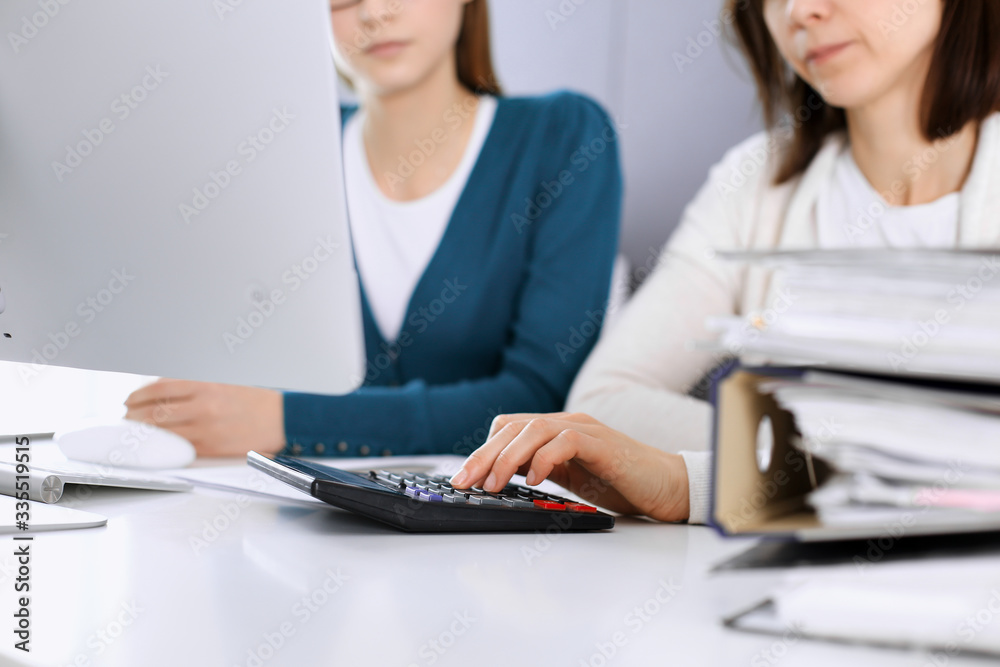 Accountant checking financial statement or counting by calculator income for tax form, hands closeup. Business woman sitting and working with colleague at the desk in office. Tax and Audit concept Accountant checking financial statement or counting by calculator income for tax form, hands closeup. Business woman sitting and working with colleague at the desk in office. Tax and Audit concept