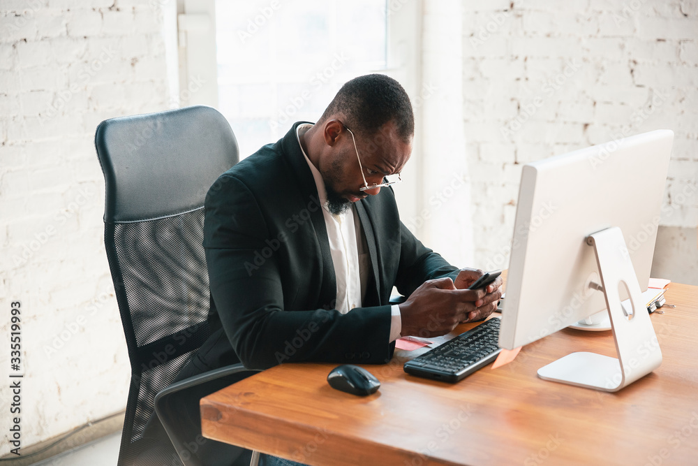 Serfing online. African-american entrepreneur, businessman working concentrated in office. Looks serios and busy, wearing classic suit, jacket. Concept of work, finance, business, success, leadership. Serfing online. African-american entrepreneur, businessman working concentrated in office. Looks serios and busy, wearing classic suit, jacket. Concept of work, finance, business, success, leadership.