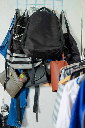 Collection of multiple backpacks, handbags and a pair of jeans stacked and hanging on a rack behind the door at home.