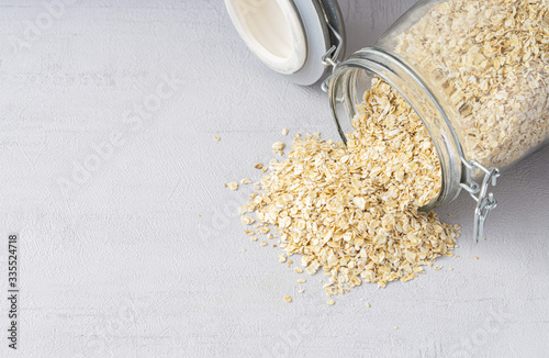 Transparent oatmeal jar with oats spread out on grey background. Copy space, close up. 